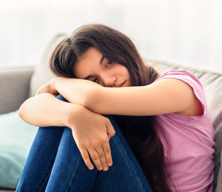 Unhappy teen girl feeling depressed or desperate, sitting on couch at home, suffering from problem or teenage depression Unhappy teen girl feeling depressed or desperate, sitting on couch at home. Indian asdolescent having difficult times, suffering from problem or teenage depression, indoors