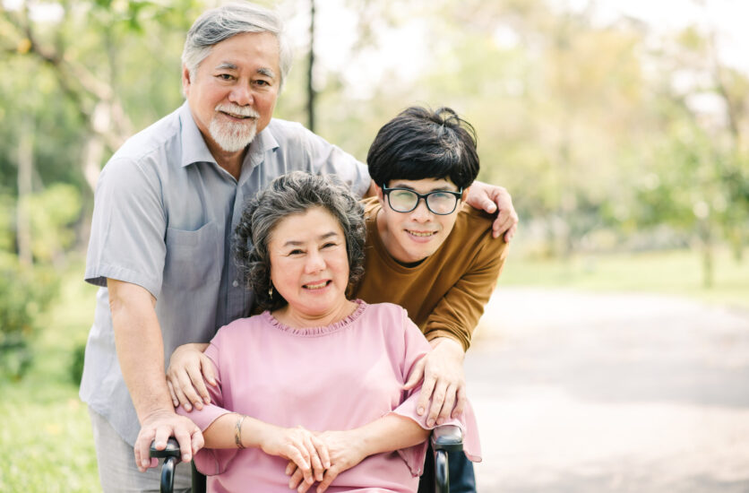 Happy Asian family with young man and senior man and woman Happy Asian family with young man and senior man and woman in wheelchair embeacing each other in the park